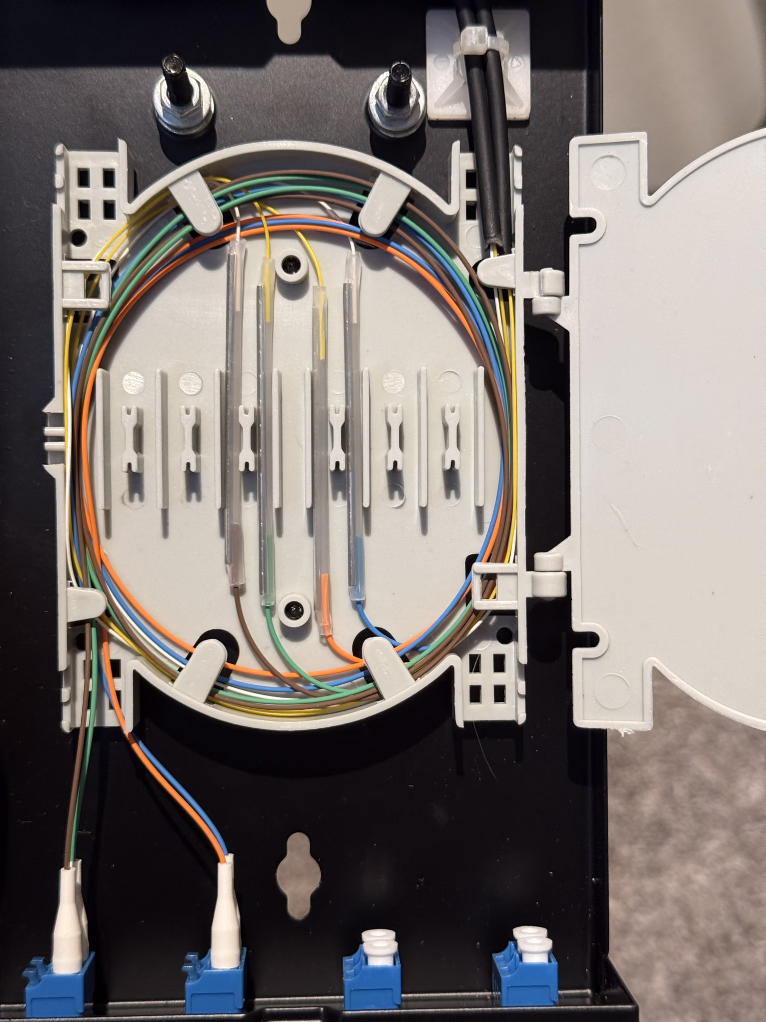 Fiber enclosure with the splice tray swung open, buffered fibers coiled and pigtails landing on LC couplers